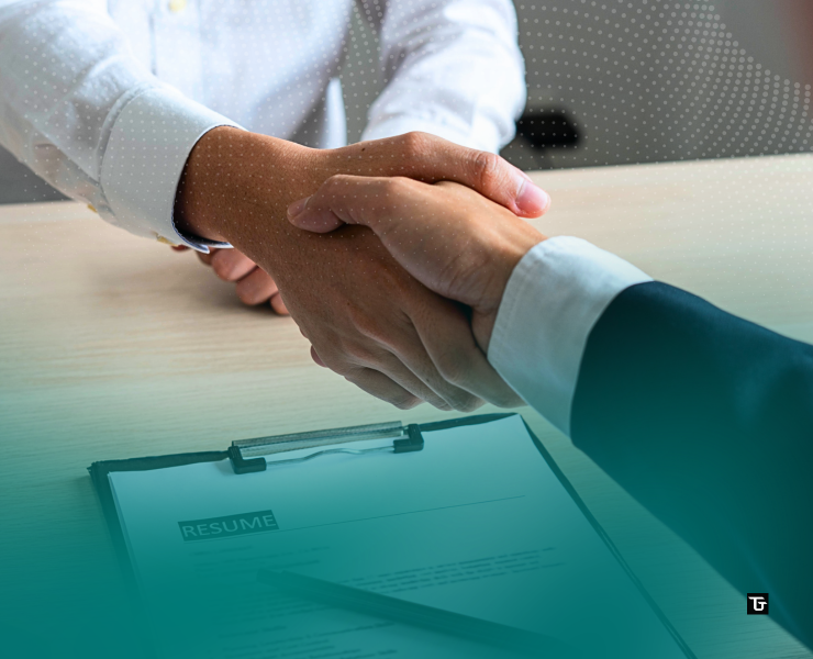 Close-up of a recruiter and job candidate shaking hands across a desk, with a résumé and clipboard visible in the foreground, symbolizing a successful hiring agreement.
