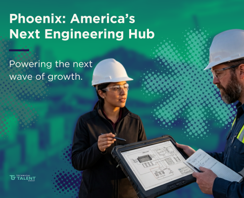 A female and male engineer in hard hats reviewing digital blue prints on a tablet at a Phoenix industrial site with energy storage units and the city skyline in the background.